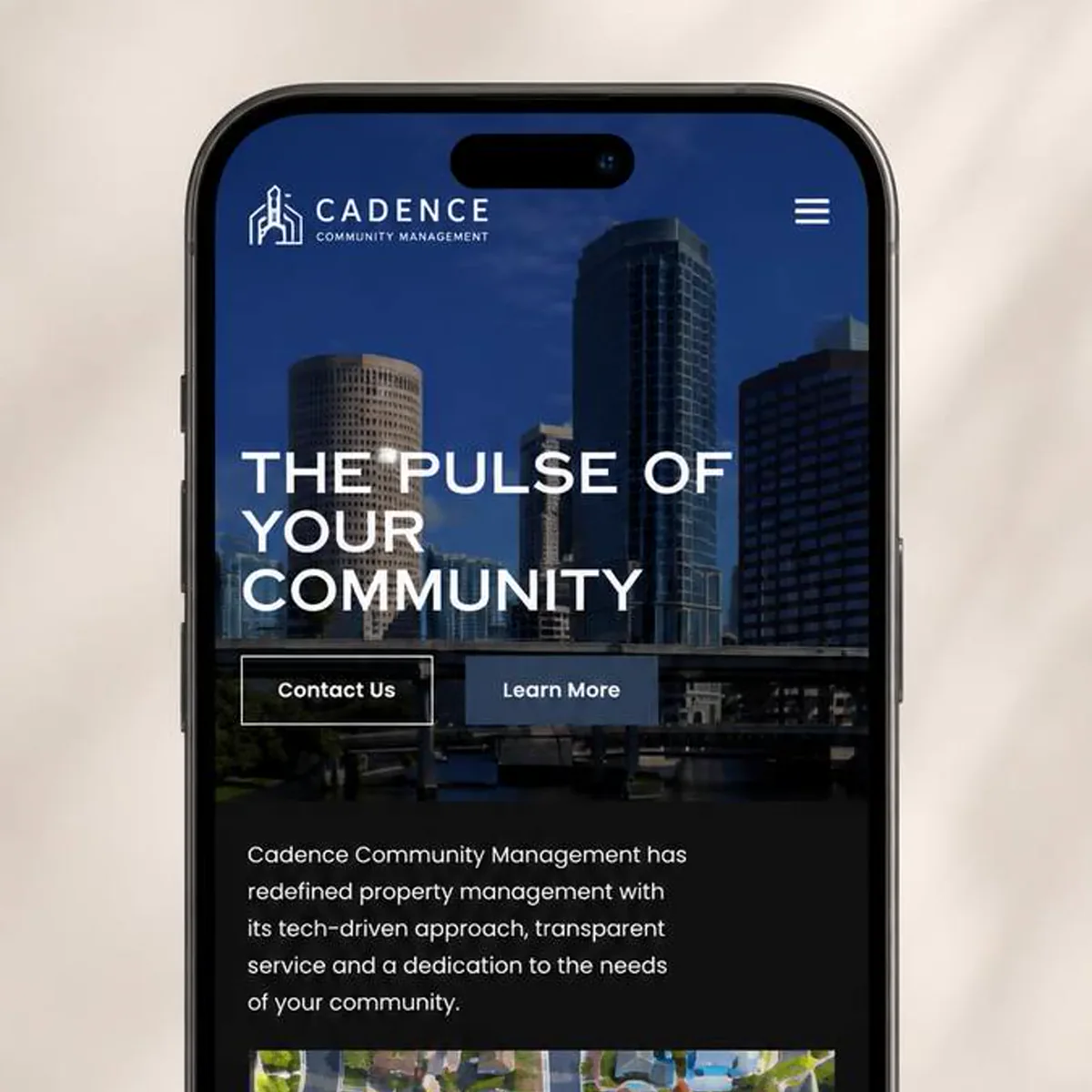 A smartphone standing upright against a warm sand-colored background, showing the home page of a property management website. A full-width downtown skyline photograph fills the top of the screen behind a large white headline, with a Contact Us button and a Learn More button side by side beneath it, and a short intro paragraph on a black section below.