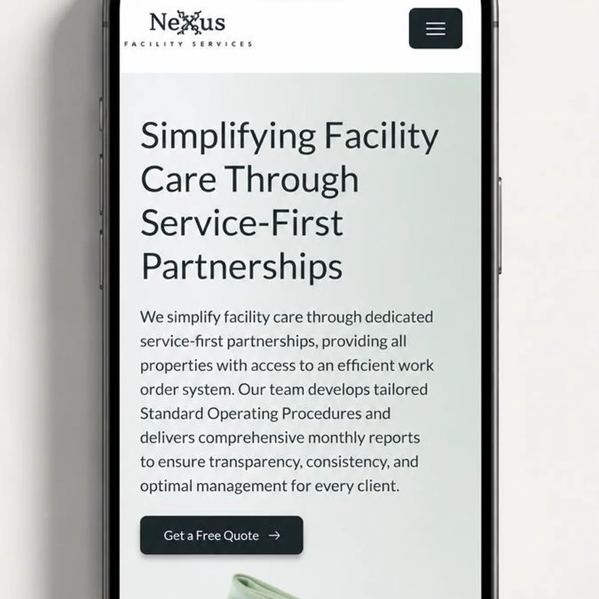 A smartphone propped against a pale grey wall displays the home page of a facility services company. A white header carries a wordmark and a dark square menu button, and below it on a soft sage background sit a large four-line headline about simplifying facility care through service-first partnerships, a short paragraph of body text, and a dark rounded button reading 