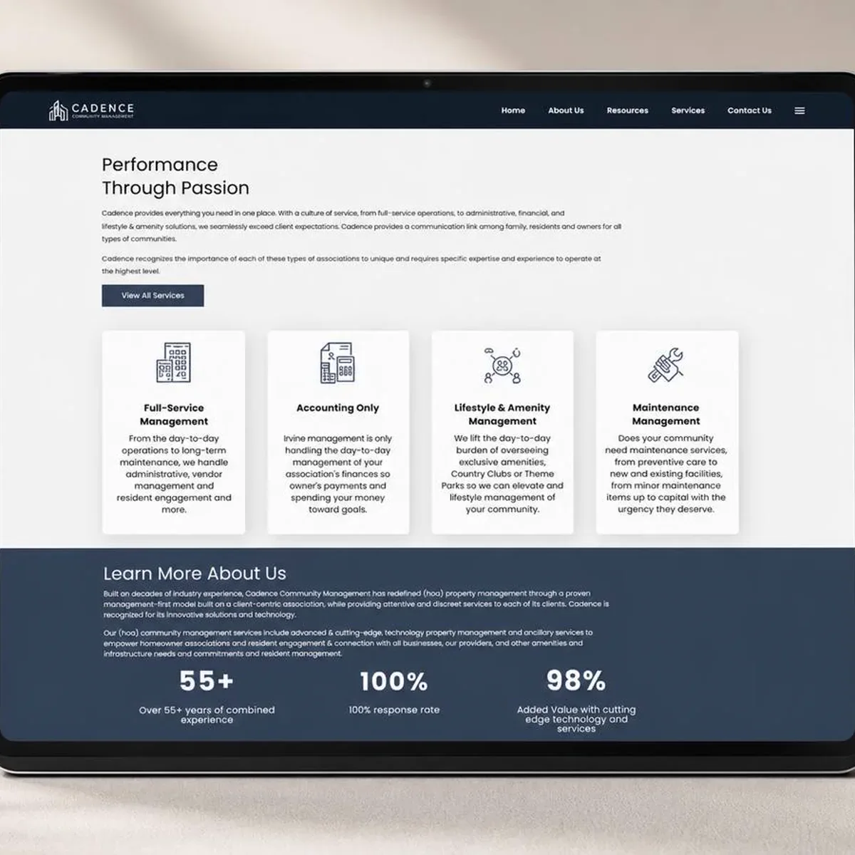 A tablet propped on a warm sand-colored surface under soft leaf shadow, showing a finished website page: a two-line headline, a short paragraph, a dark rectangular button, a row of four white cards with line-drawn icons and short service descriptions, and beneath them a deep navy band carrying three large statistics.