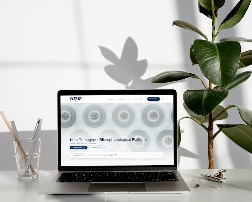 A laptop on a bright desk beside a plant, showing the HTMP Biotechnology platform page